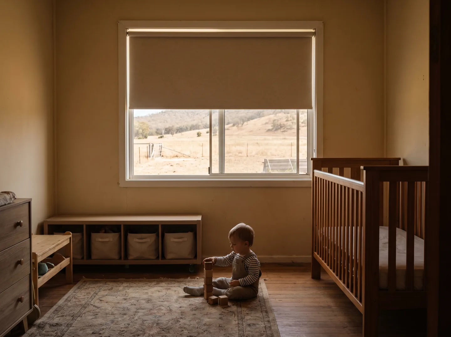 A child playing on the floor of a bedroom fitted with a cordless roller blind, no hanging cords